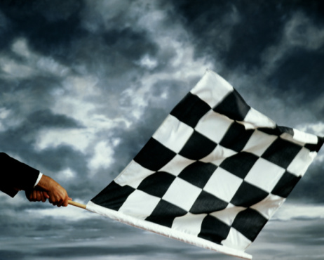 Hands waving black and white chequered flag, cloudy sky in back ground